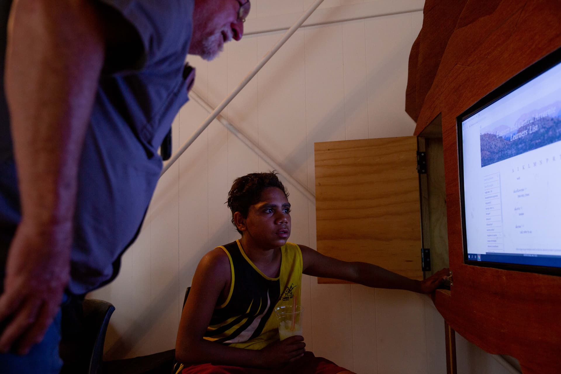 A young person using a touchscreen while an older man stands nearby inside a learning space.