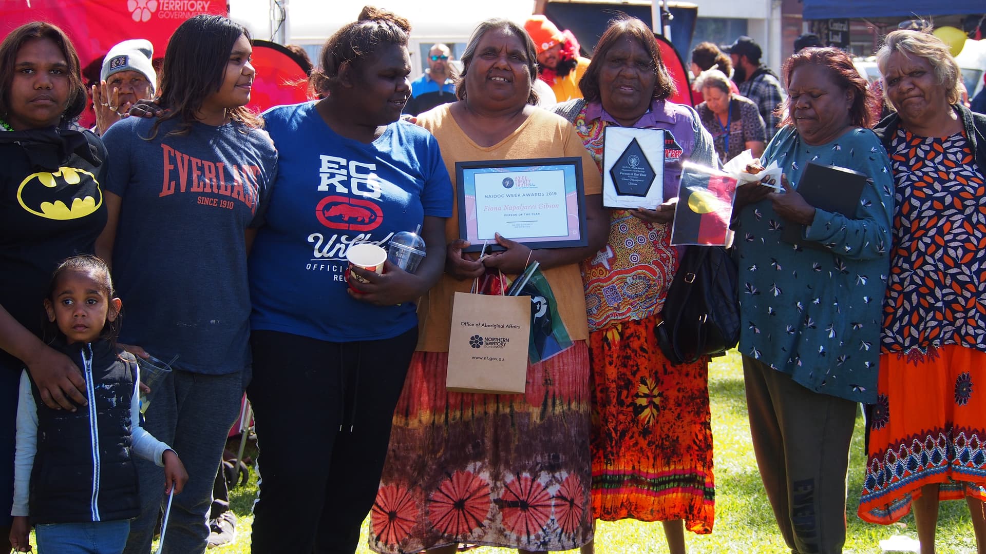 A group of women and children standing together outdoors with awards and certificates.