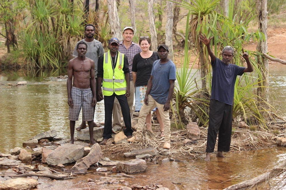 A group of collaborators standing beside a creek among pandanus and rocks.